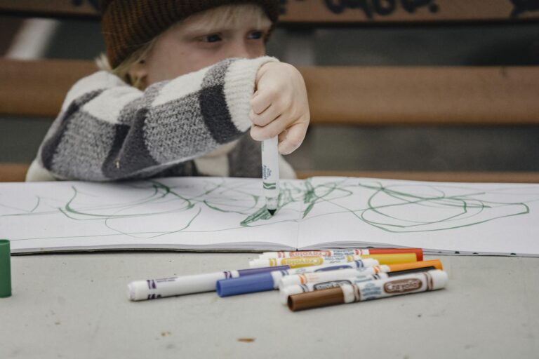 A young child concentrates while drawing with colorful markers in a sketchbook, showcasing creativity.