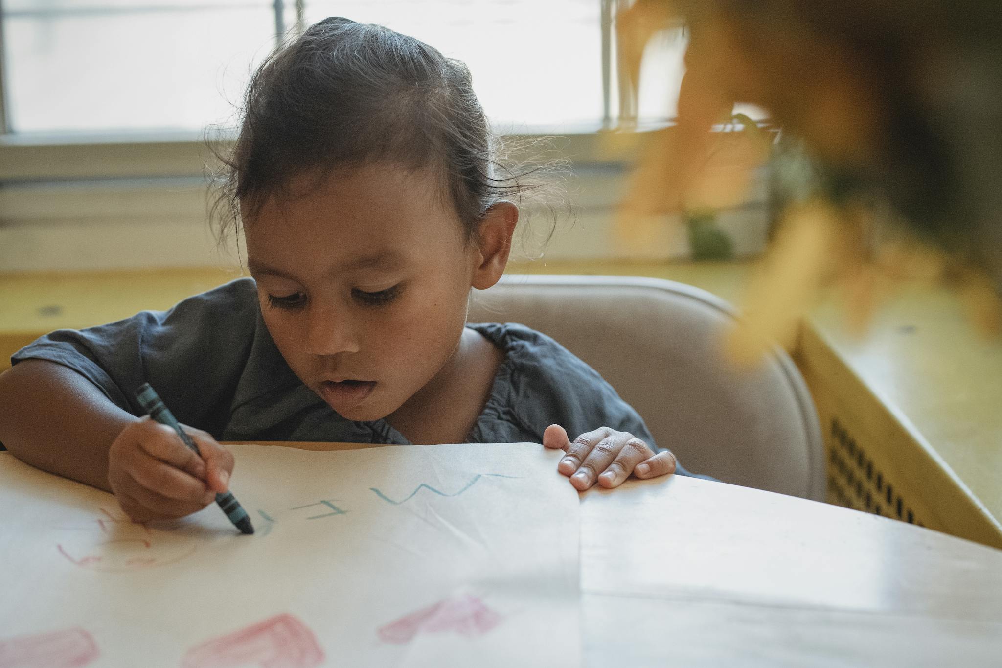 A young girl focused on drawing with crayons, depicting childhood creativity and learning indoors.